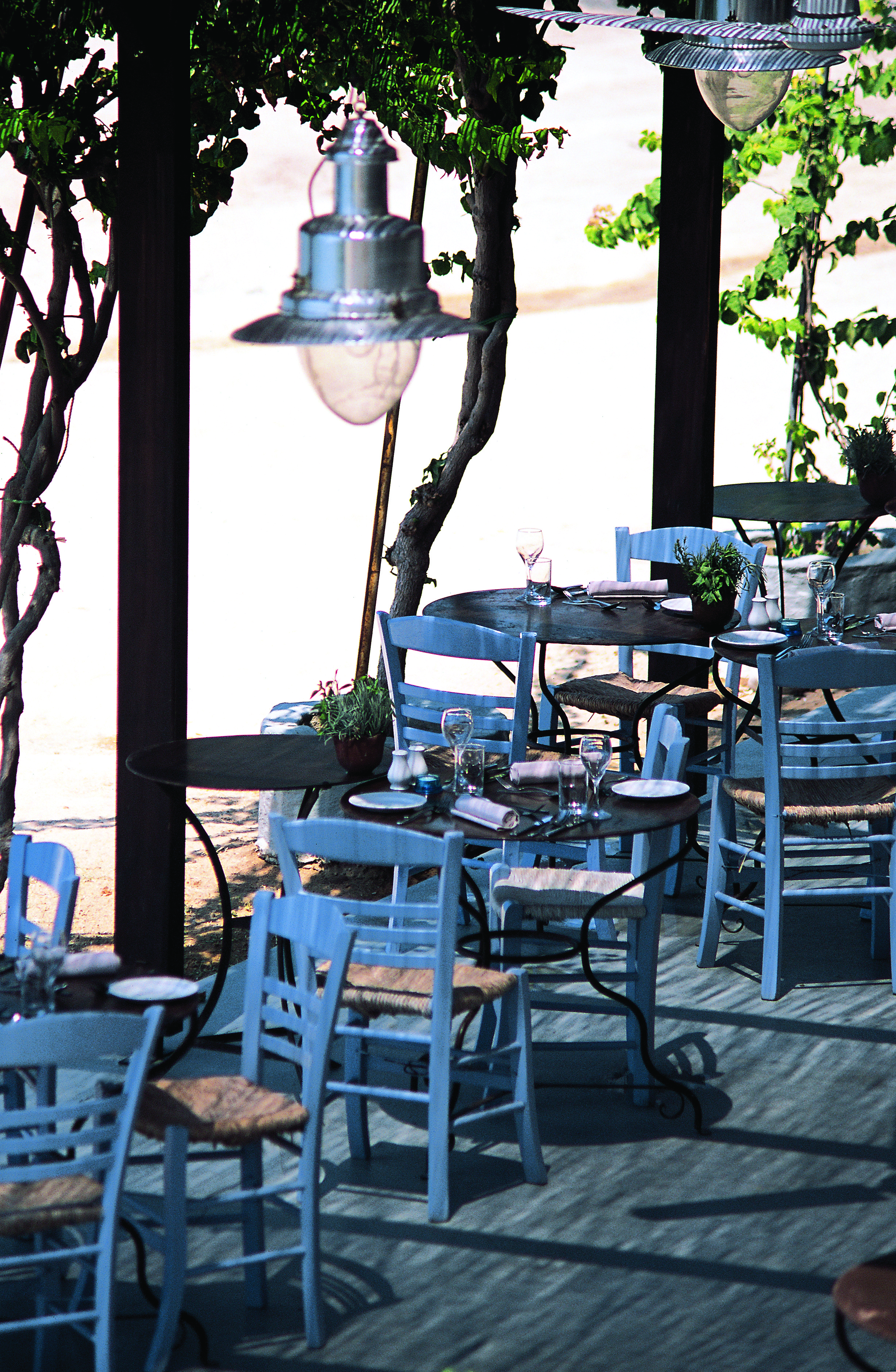 Outdoor dining terrace with white and wooden tables and chairs set out 