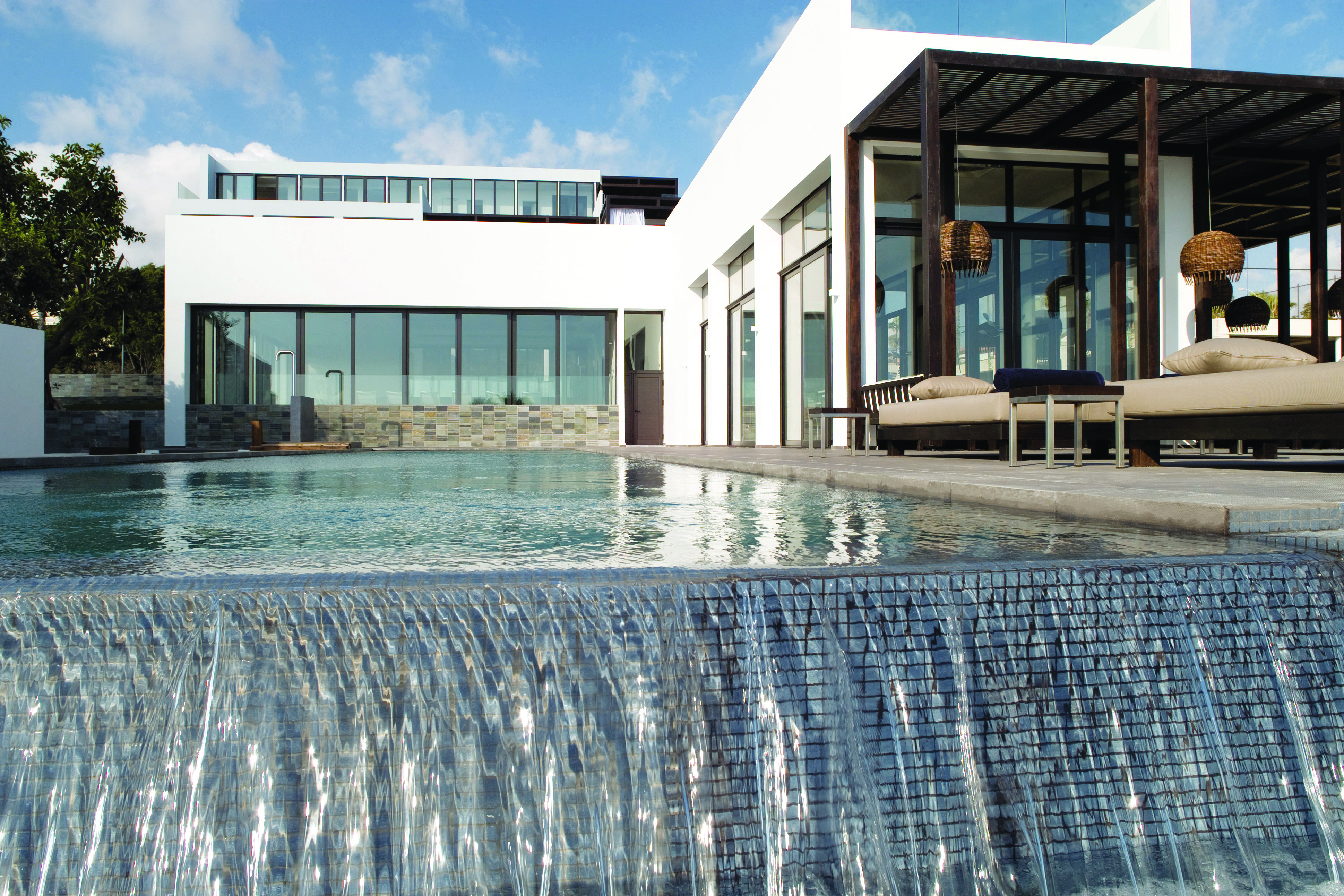 View from the end of the hotel pool with a mini waterfall, looking onto white stone hotel