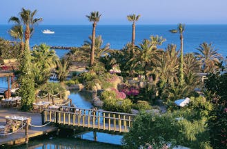 Annabelle Hotel Cyprus exterior panorama of hotel grounds with palm trees flowers and a bridge with sea views