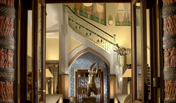 Entrance to hotel with high ceiling, large chandelier and statues
