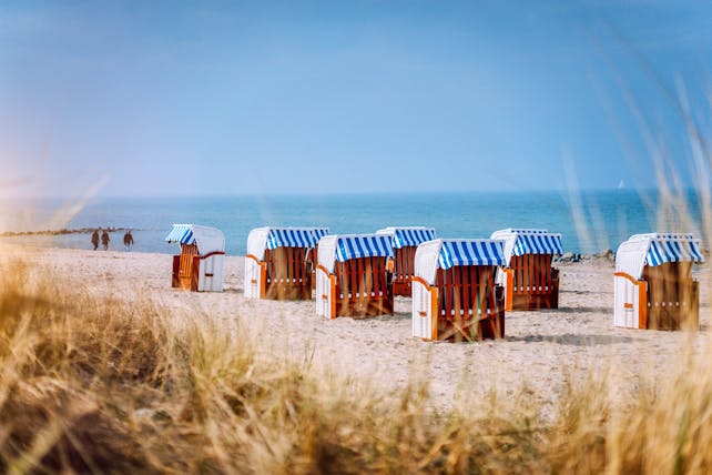 Blue striped roofed chairs on sandy beach by dunes at Travemunde