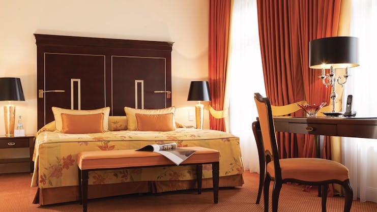 Deluxe double room at the Hotel Bulow Palais with an orange colour scheme, large double bed, red curtains and wooden bed frame
