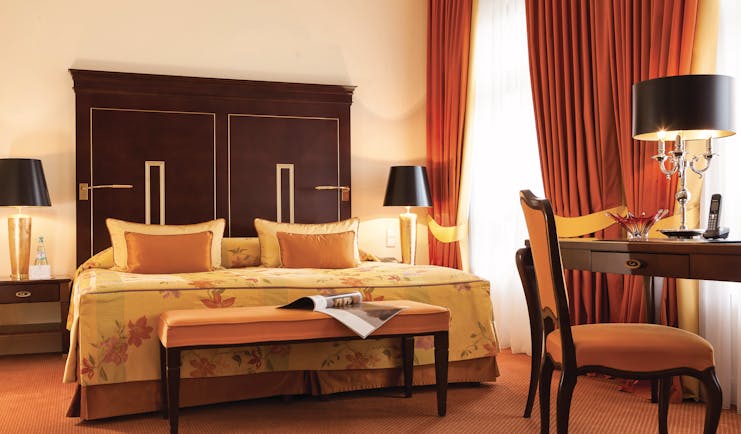Deluxe double room at the Hotel Bulow Palais with an orange colour scheme, large double bed, red curtains and wooden bed frame