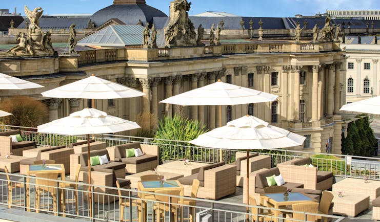 Hotel de Rome Berlin rooftop terrace with sofas and umbrellas overlooking large building overlooking the opera house