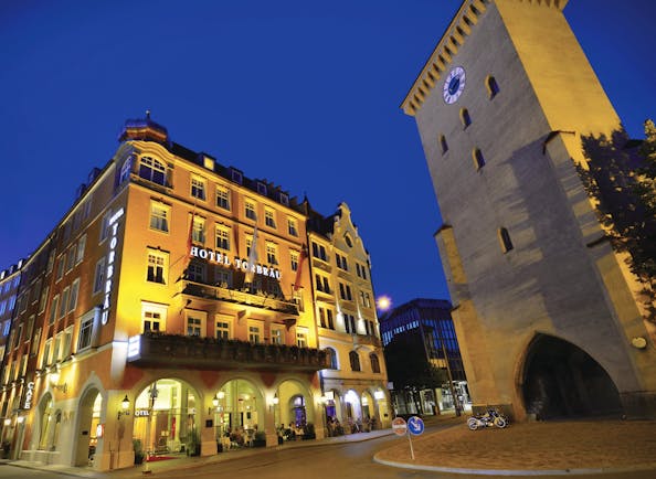 Hotel Torbrau Munich exterior night large building in front of a clock tower