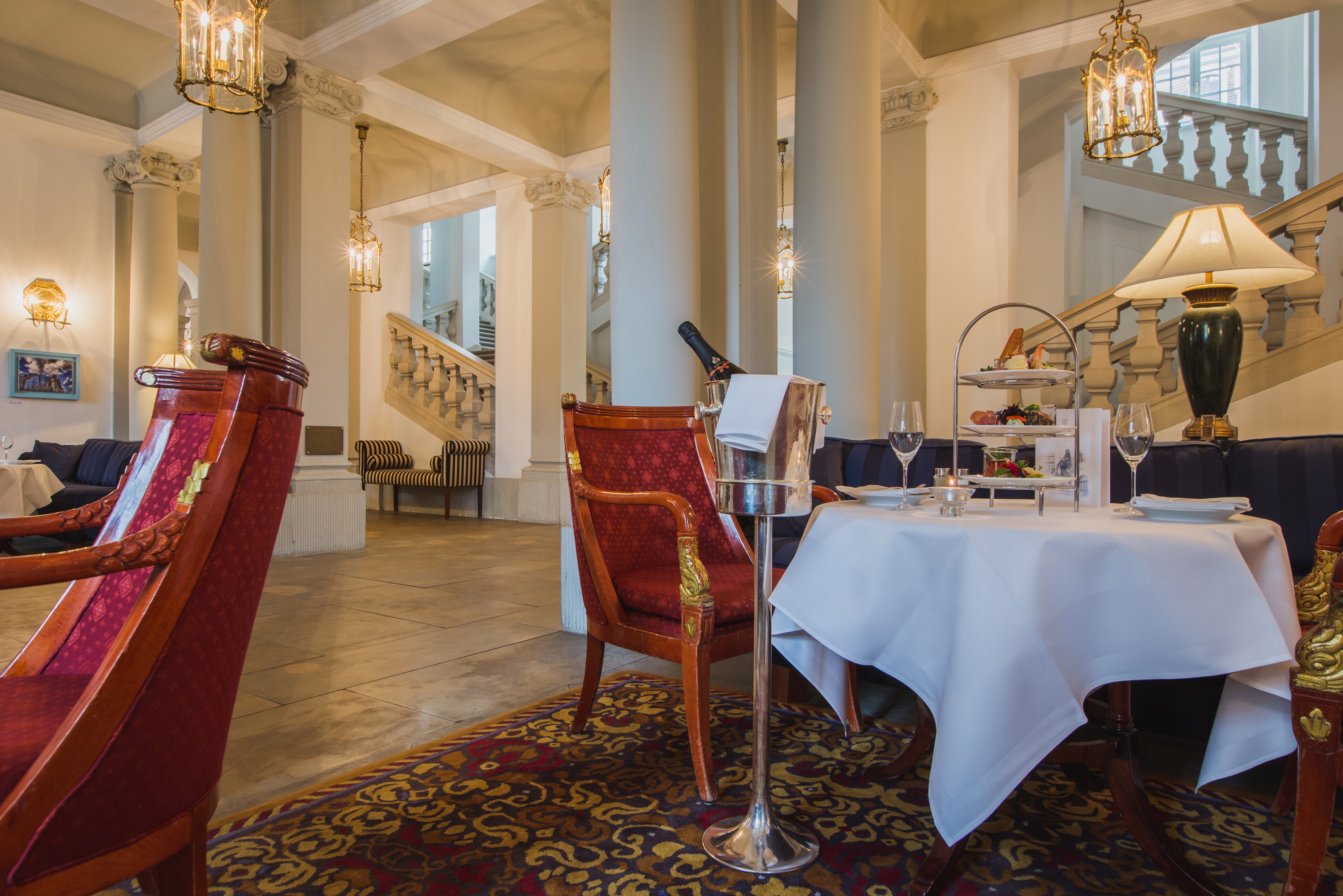 Taschenbergpalais cafe vestibul, indoor eating area, grand decor woth stone pilars and carbed staircase, table and chairs