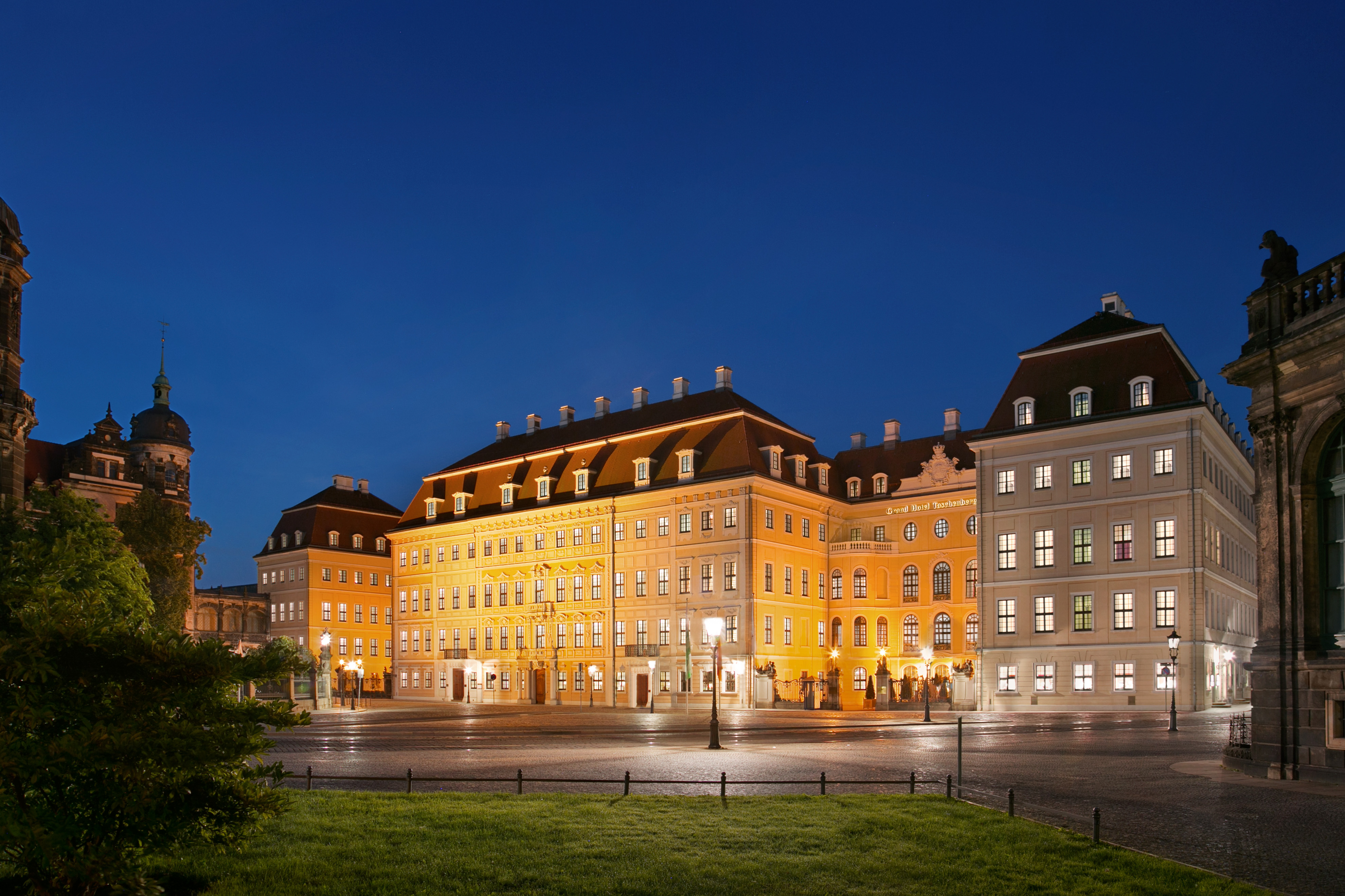 Exterior of hotel at night showing large white building with lots of small windows 