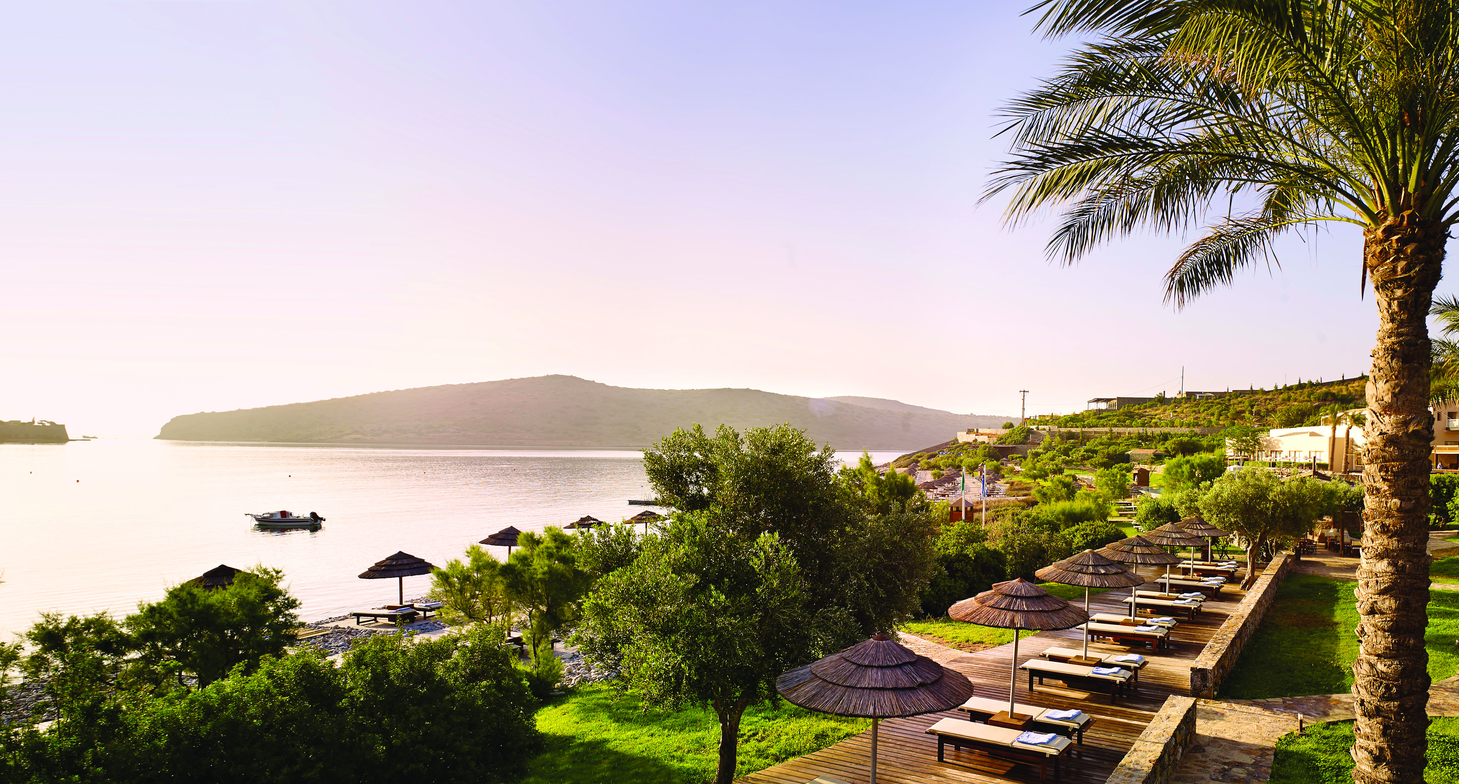 Blue Palace Greece deck terrace area with sun loungers and palm umbrellas and sea view