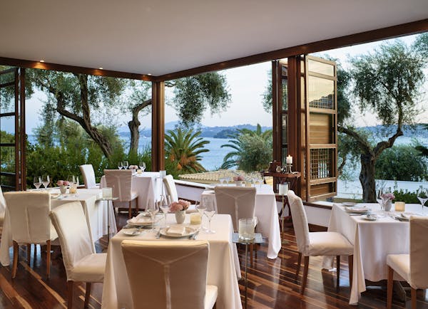 Airy restaurant with white tables and wooden floor looking onto palms