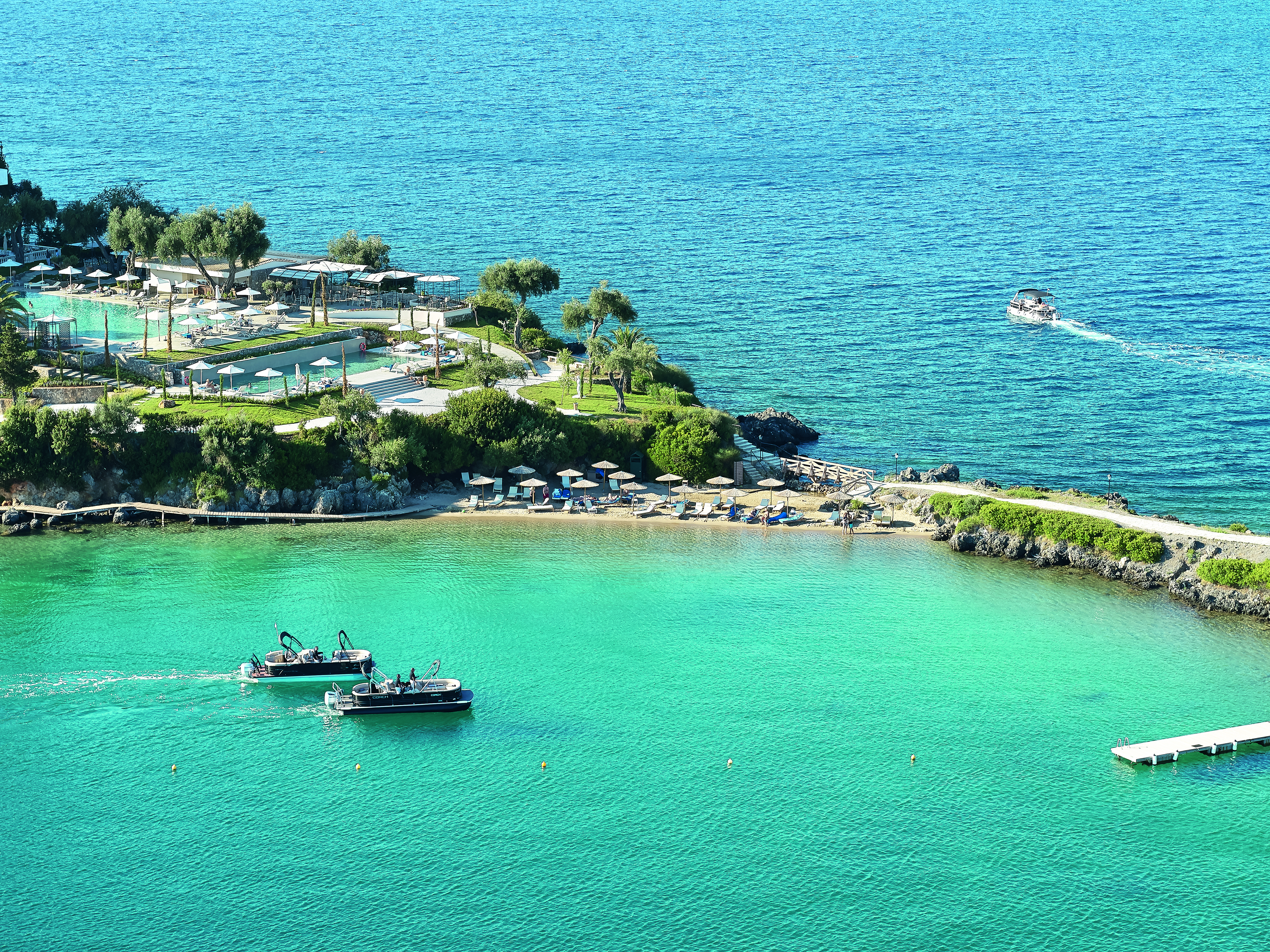 Blue waters with boats, jetty and swmming pools at the Corfu Imperial