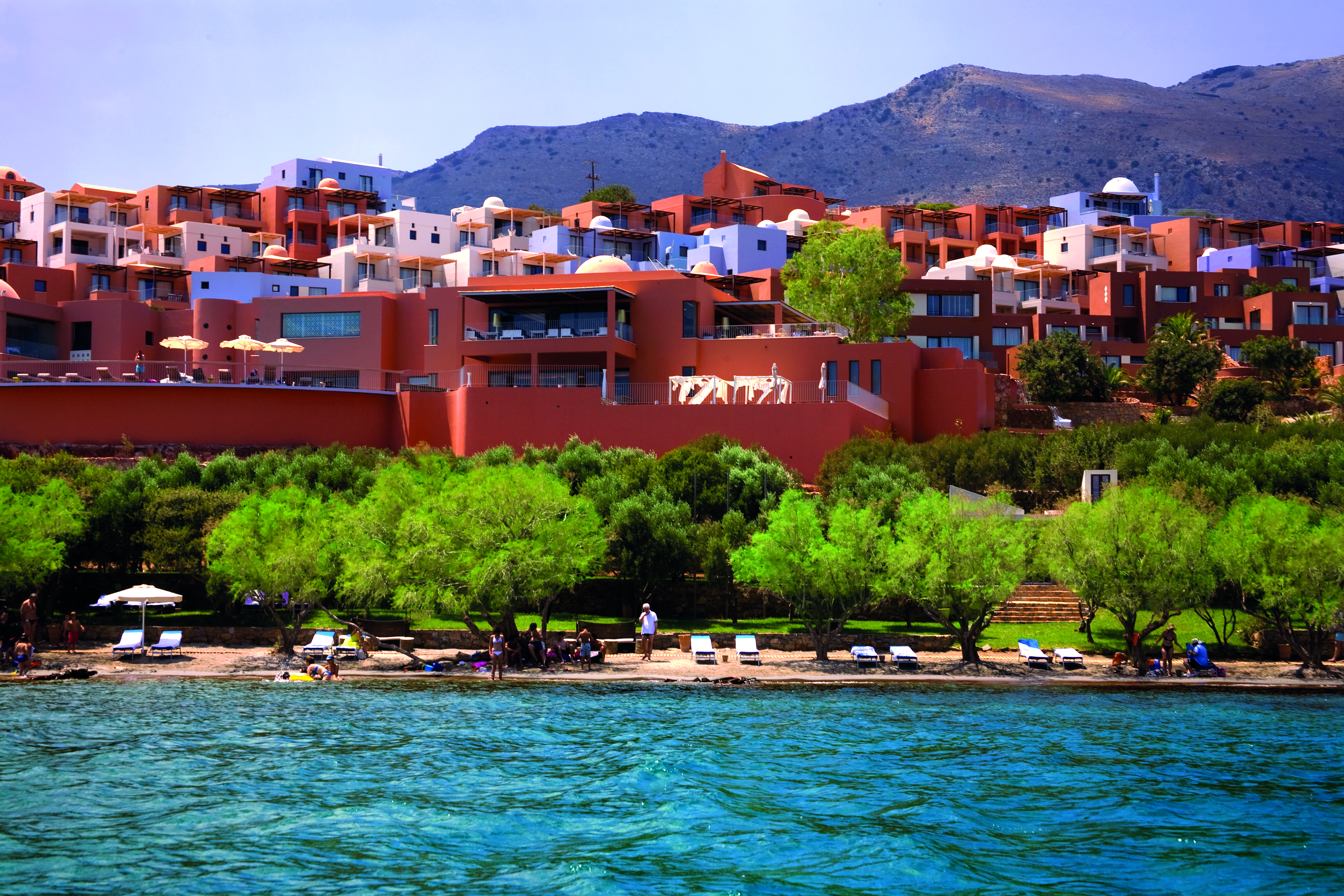 Domes of Elounda Greece exterior panorama several terracotta buildings near hills and a beach