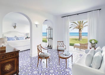 Grecotel Caramel Greece  beach villa bedroom with blue and white tiled floor sitting area and doors opening to garden 