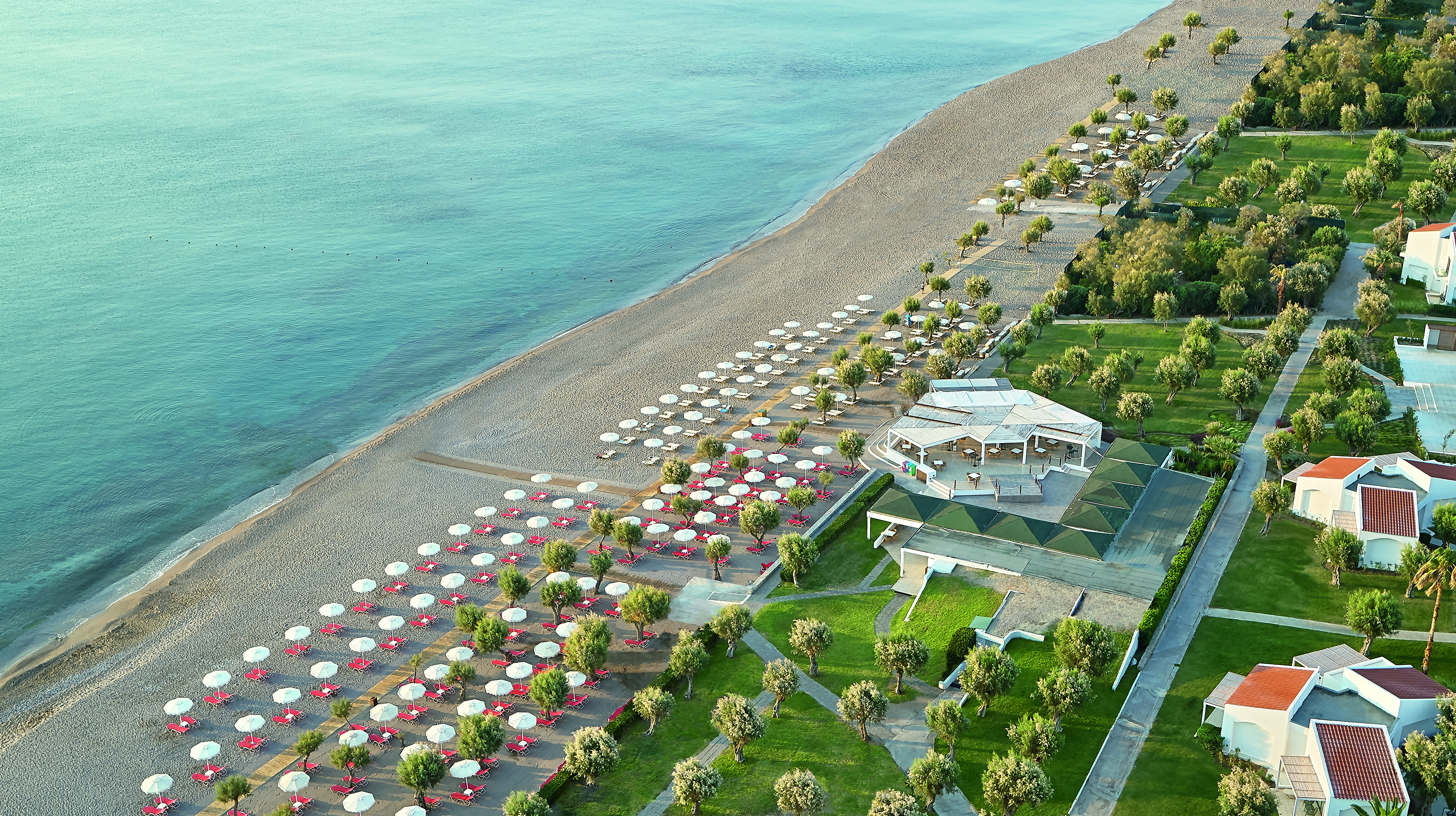 Long sandy beach with umbrellas flanked by grass