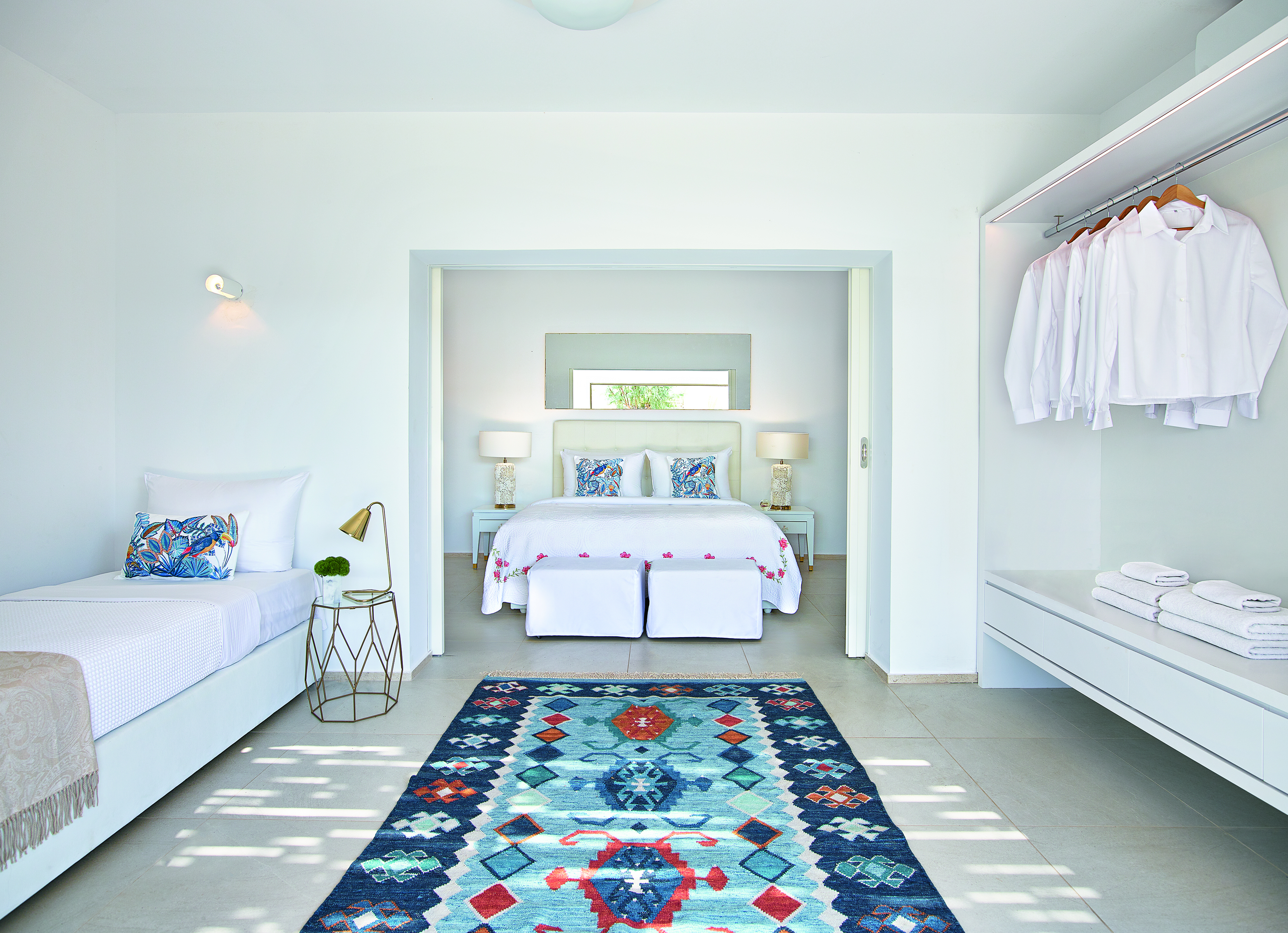 Large white room with extra bed and open wardrobe with blue rug
