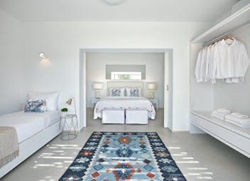 Large white room with extra bed and open wardrobe with blue rug