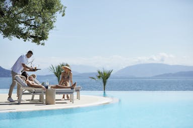 Ikos Dassia Greece outdoor pool couple being served a drink at outdoor pool with sea view