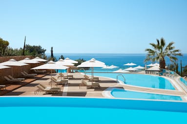 Ikos Oceania Greece infinity pool with white umbrellas and sun loungers