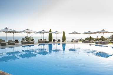 Ikos Oceania Greece outdoor swimming pool with sun loungers umbrellas and sea view