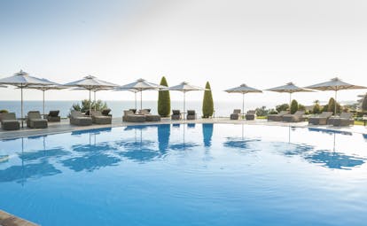Ikos Oceania Greece outdoor swimming pool with sun loungers umbrellas and sea view