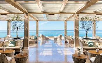 Ikos Oceania Greece veranda restaurant outdoor lounge area with large windows and sea views