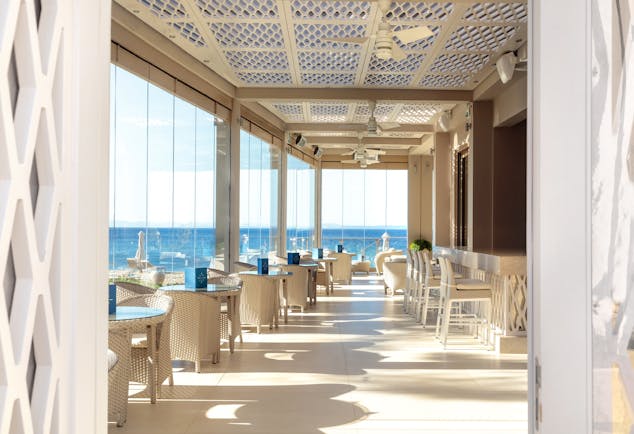 Helios bar at the Ikos Olivia with large window panneled walls looking over the ocean and white chairs and tables set up 