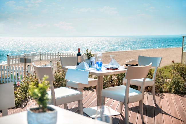 Fresco italian restaurant at the Ikos Olivia, showing an outdoor seating area on wooden decking, overlooking the beach and sea