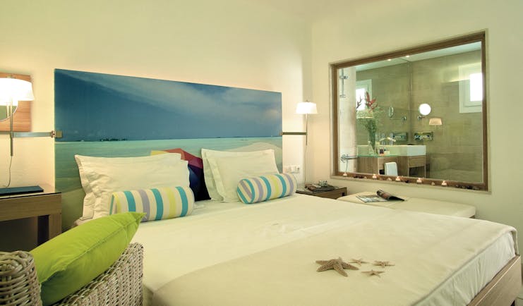 Petasos Beach Resort Greece design suite bedroom with picture of beach behind bed and window into bathroom