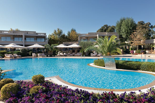 Sani Asterias Greece outdoor swimming pool next to pink and purple flowers with loungers and umbrellas