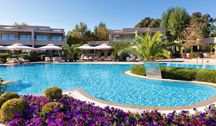 Sani Asterias Greece outdoor swimming pool next to pink and purple flowers with loungers and umbrellas