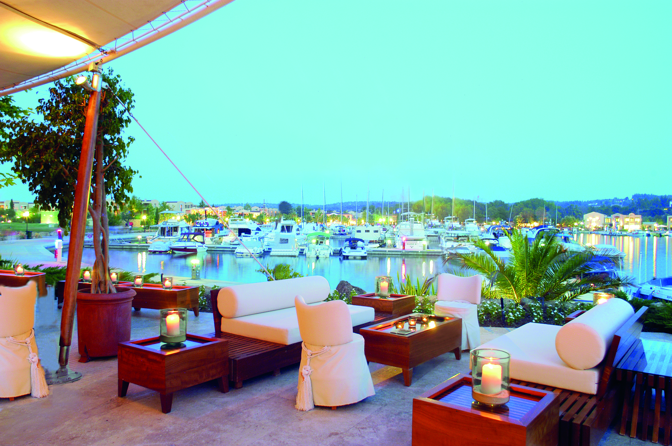 Sani Asterias Greece terrace bar outdoor lounge area with sofas next to boats docked in marina