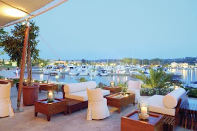 Sani Asterias Greece terrace bar outdoor lounge area with sofas next to boats docked in marina