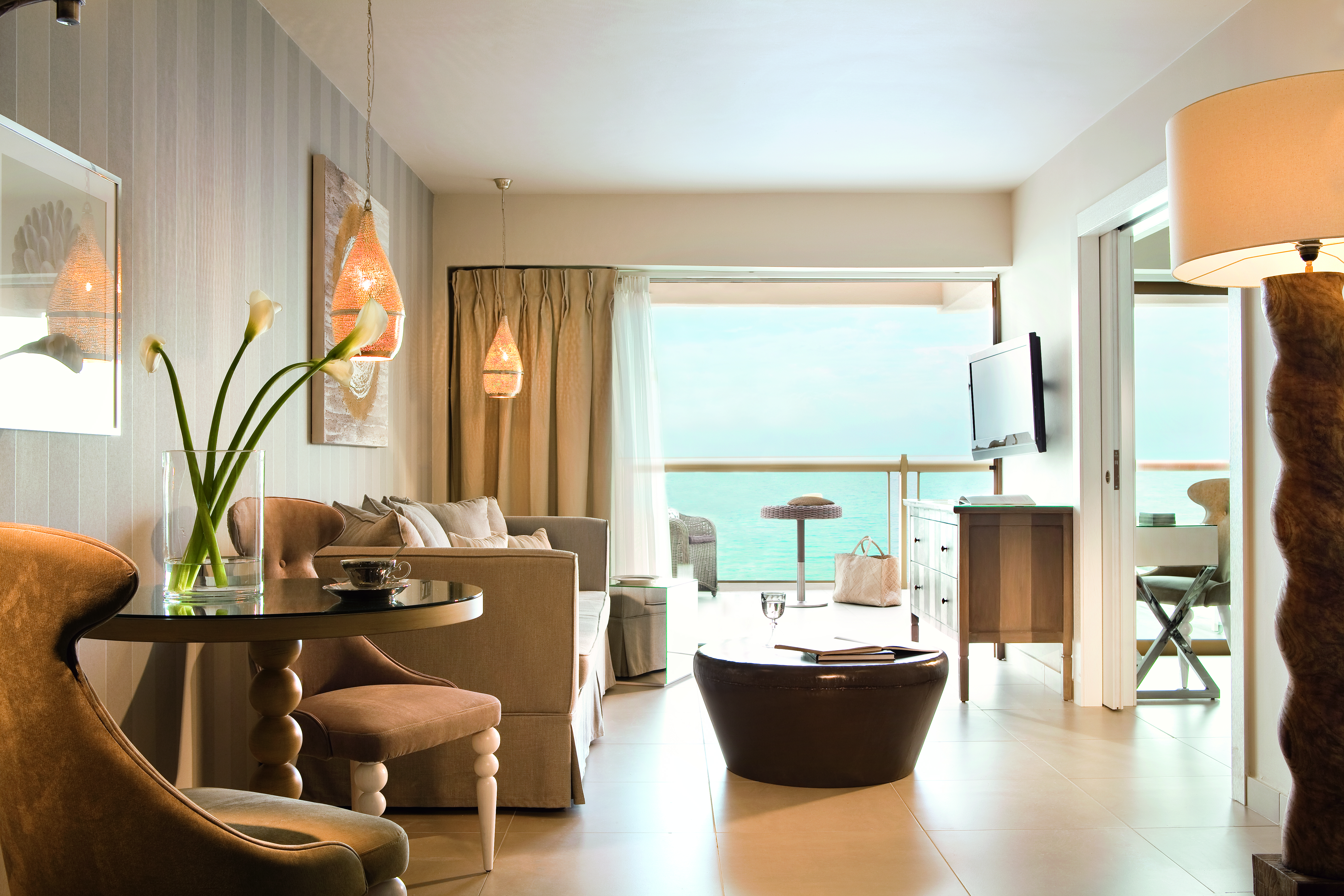 Lounge in a Sani Beach family room with a balcony looking over the sea, paintings on the walls and a sofa