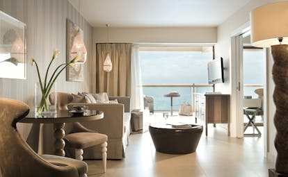 Lounge in a Sani Beach family room with a balcony looking over the sea, paintings on the walls and a sofa