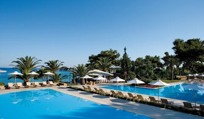 Sani Club Greece outdoor pool loungers umbrellas palm trees sea view