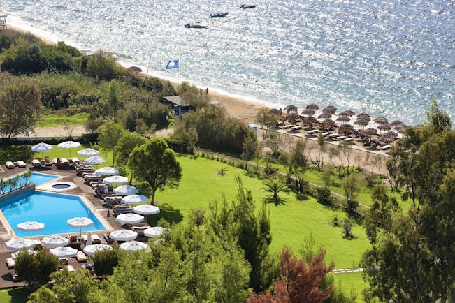 Overview of the Skiathos Princess hotel showing a large pool surrounded by white umbrellas and deck chairs. The beach is shown in close proximity
