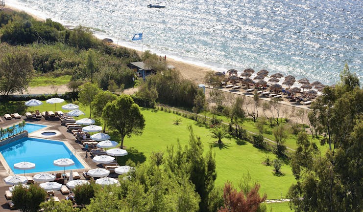 Overview of the Skiathos Princess hotel showing a large pool surrounded by white umbrellas and deck chairs. The beach is shown in close proximity