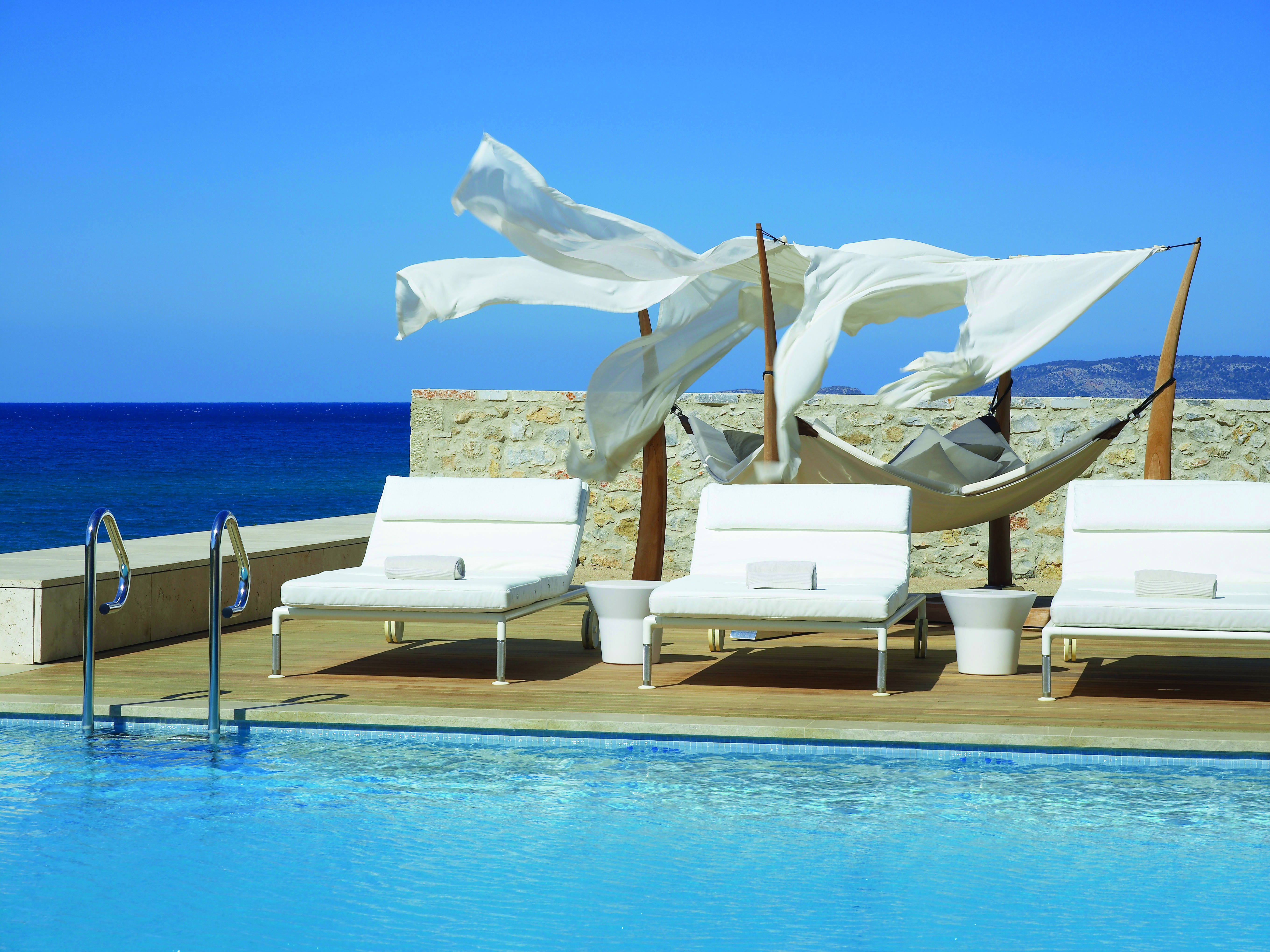 The Romanos Greece outside swimming pool with decked area with loungers and a hammock and sea view