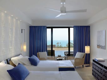 The Romanos Greece twin bedroom with blue curtains and patio doors to terrace