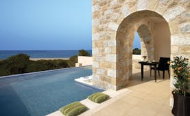 View of an outdoor infinity pool with green cushions on the pool edge and a stone arch walk-way 
