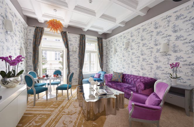 Aria Hotel Budapest suite sitting room  orange chandelier purple sofa and chair blue chaise longue table and blue chairs 