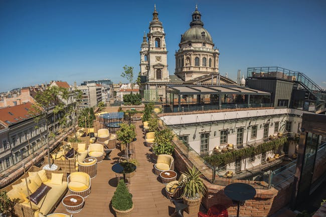 Aria Hotel Budapest rooftop terrace with yellow and brown chairs pot plants and view over a courtyard and cathedral
