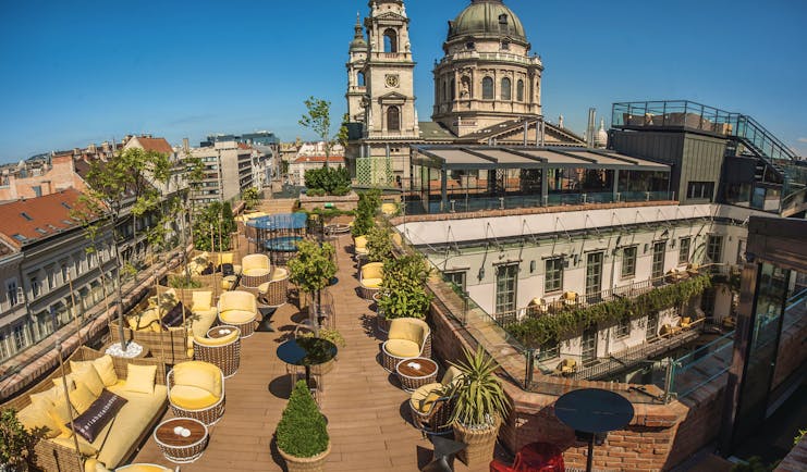 Aria Hotel Budapest rooftop terrace with yellow and brown chairs pot plants and view over a courtyard and cathedral