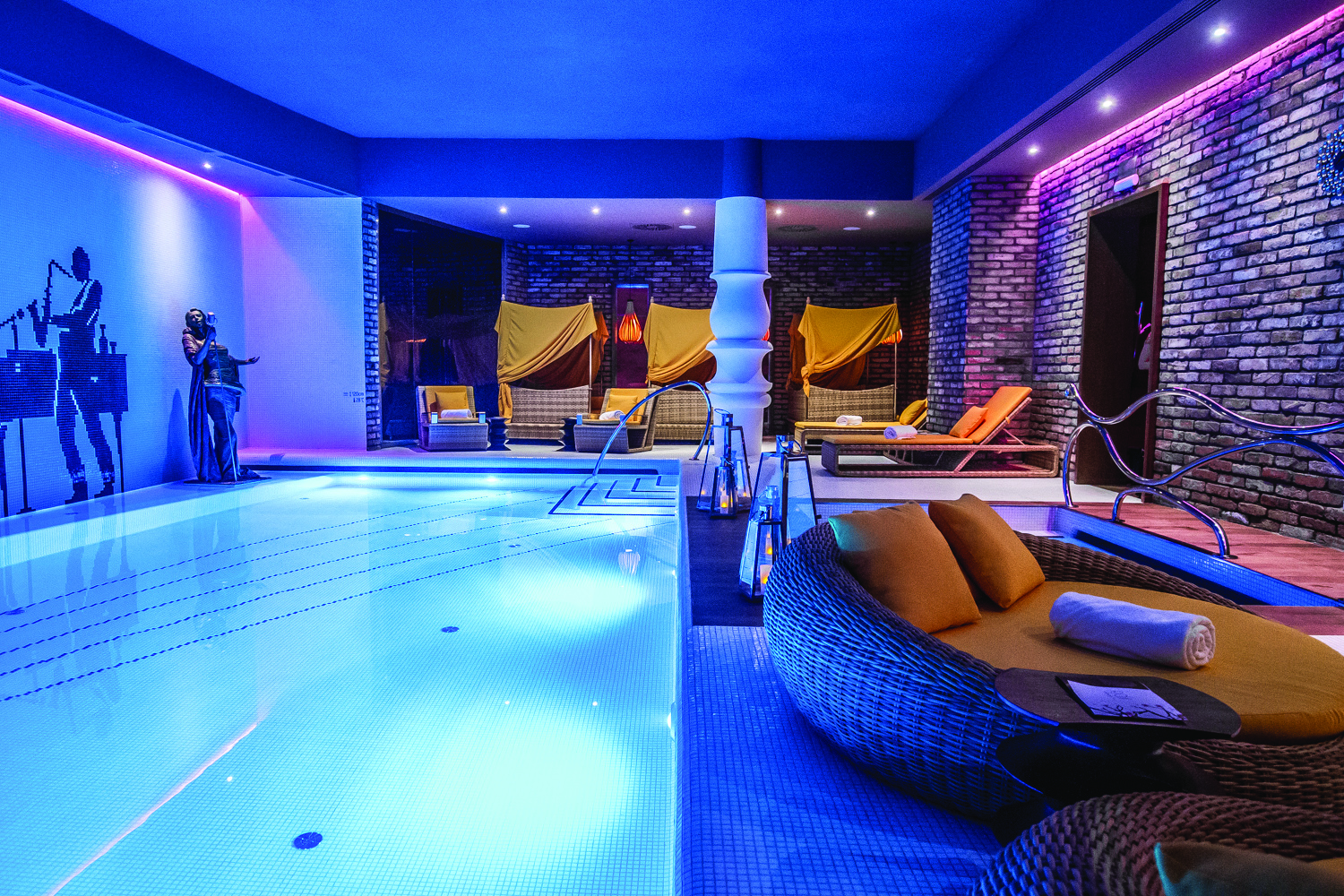 Aria Hotel Budapest indoor pool a mural of a jazz player a round sofa and yellow cabanas