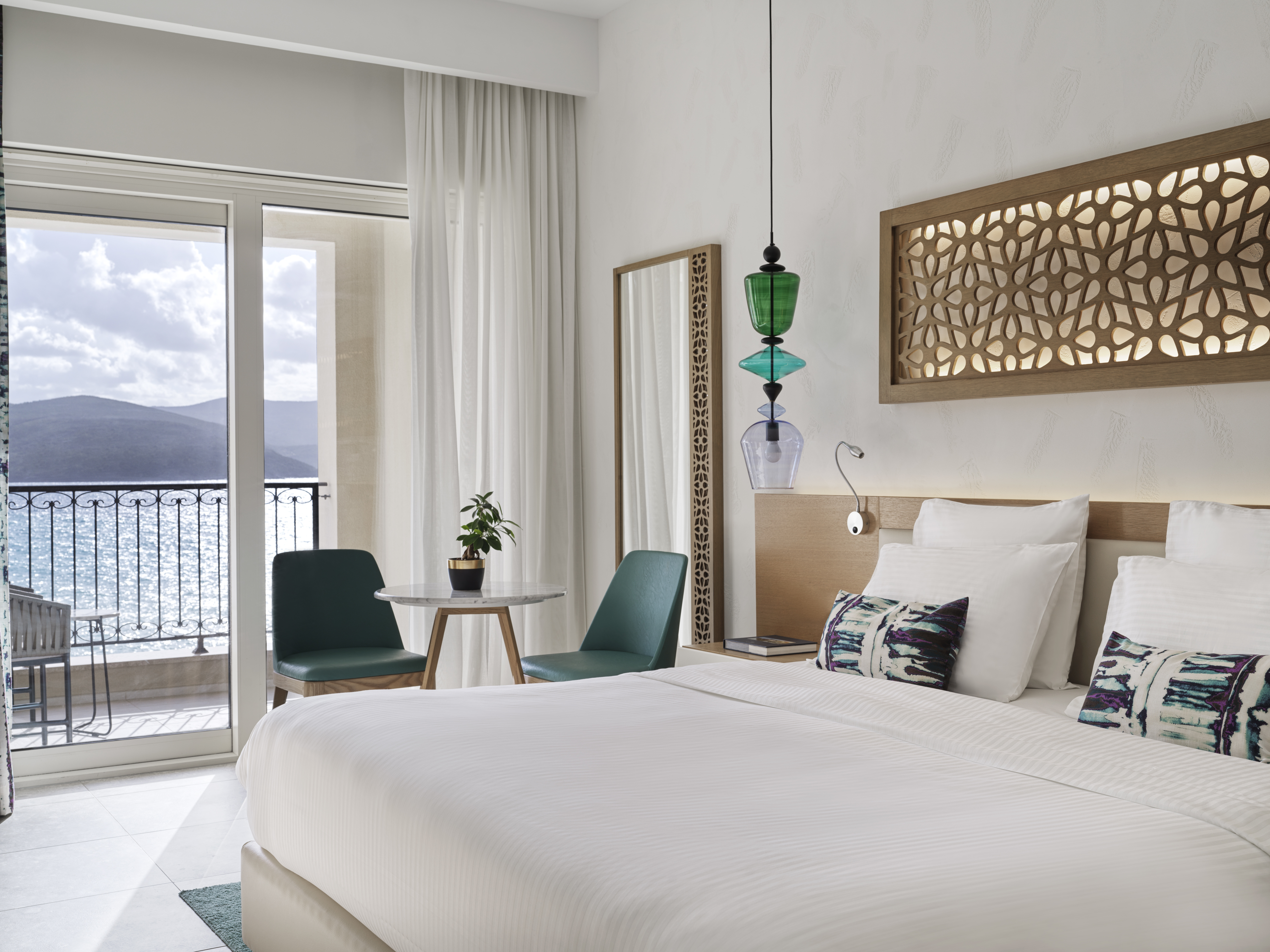 Chedi Lustica Bay room with white walls and linens, turquoise chairs and light wood touches, and balcony with sea views