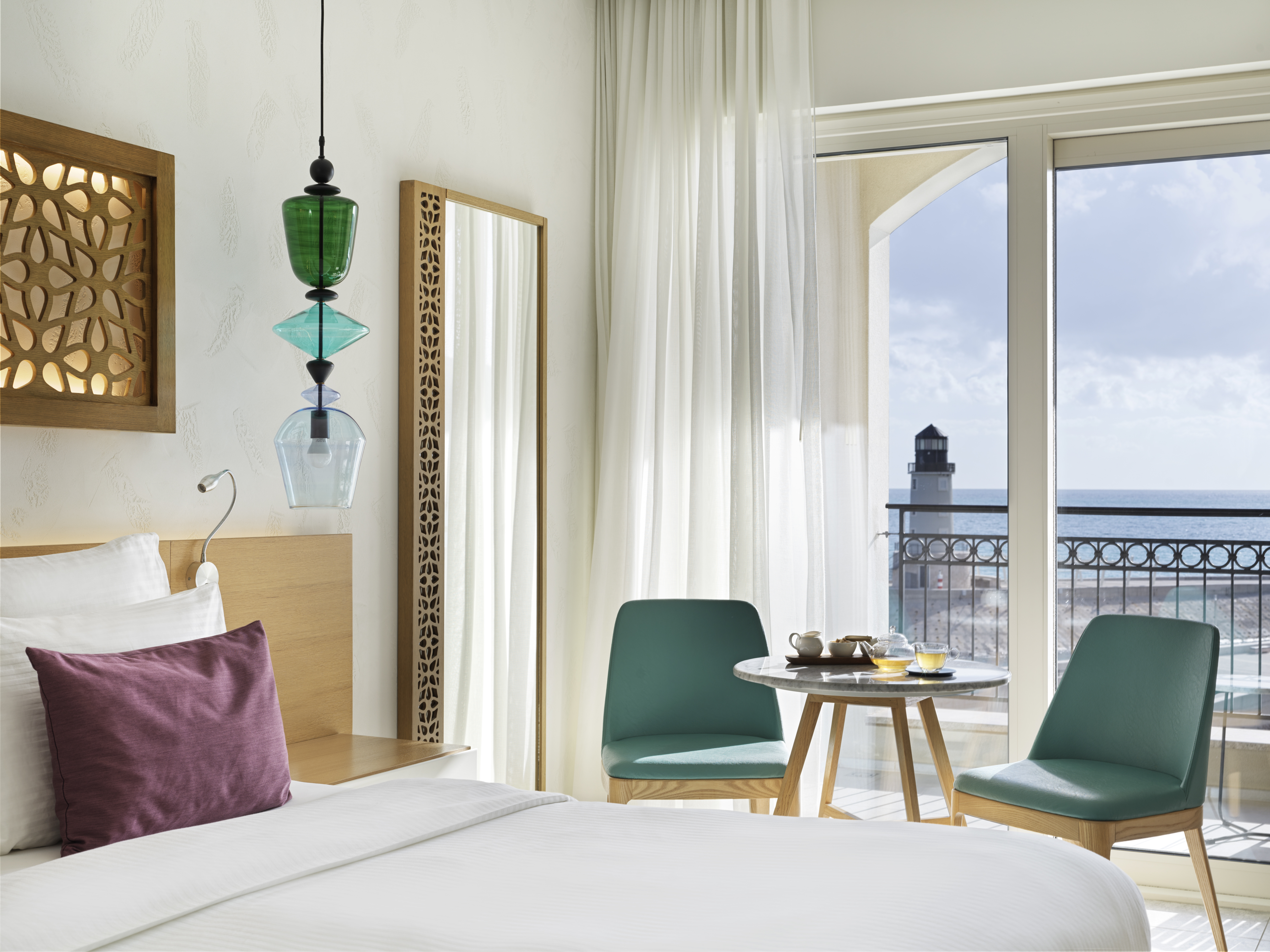 Chedi Lustica Bay room with white linens and pops of purple and turquoise, and views of the marina from the balcony and double doors