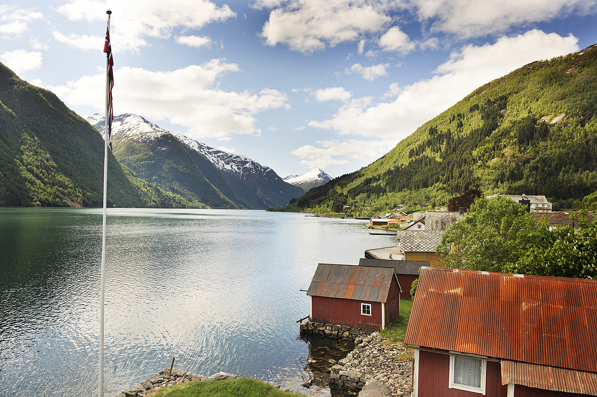 Fjaerland Fjordstove Hotell lake with flagpole and small cabins with red roofs by side