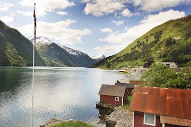 Fjaerland Fjordstove Hotell lake with flagpole and small cabins with red roofs by side