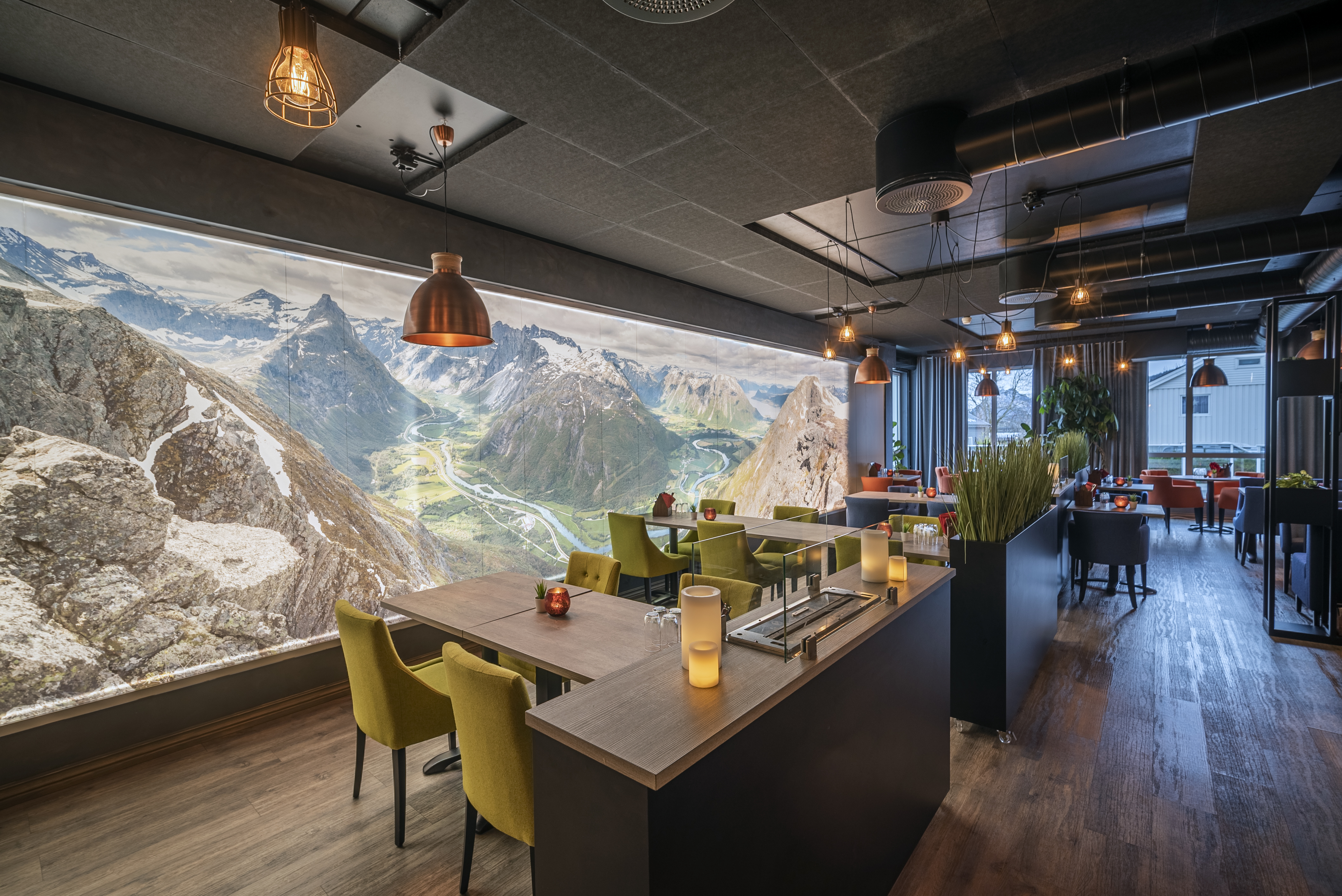 Grand Hotel Andalsnes restaurant, showing a backlit mountain scene on the wall beside the tables and chairs, with low-hanging bronze lighting
