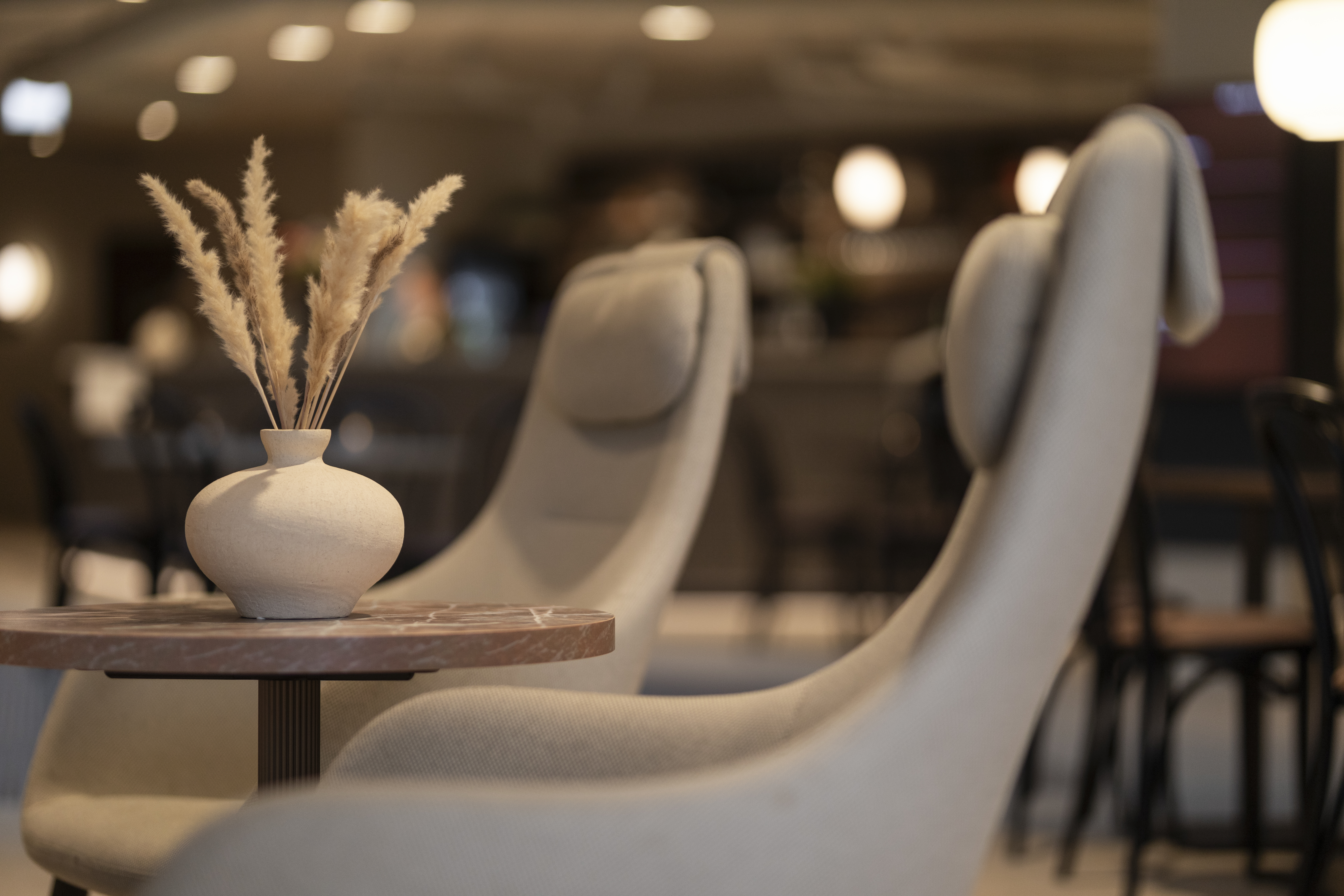 Home Hotel Grimstad lobby chairs, with smooth modern shape, arranged around a table with clay vase and dried flowers
