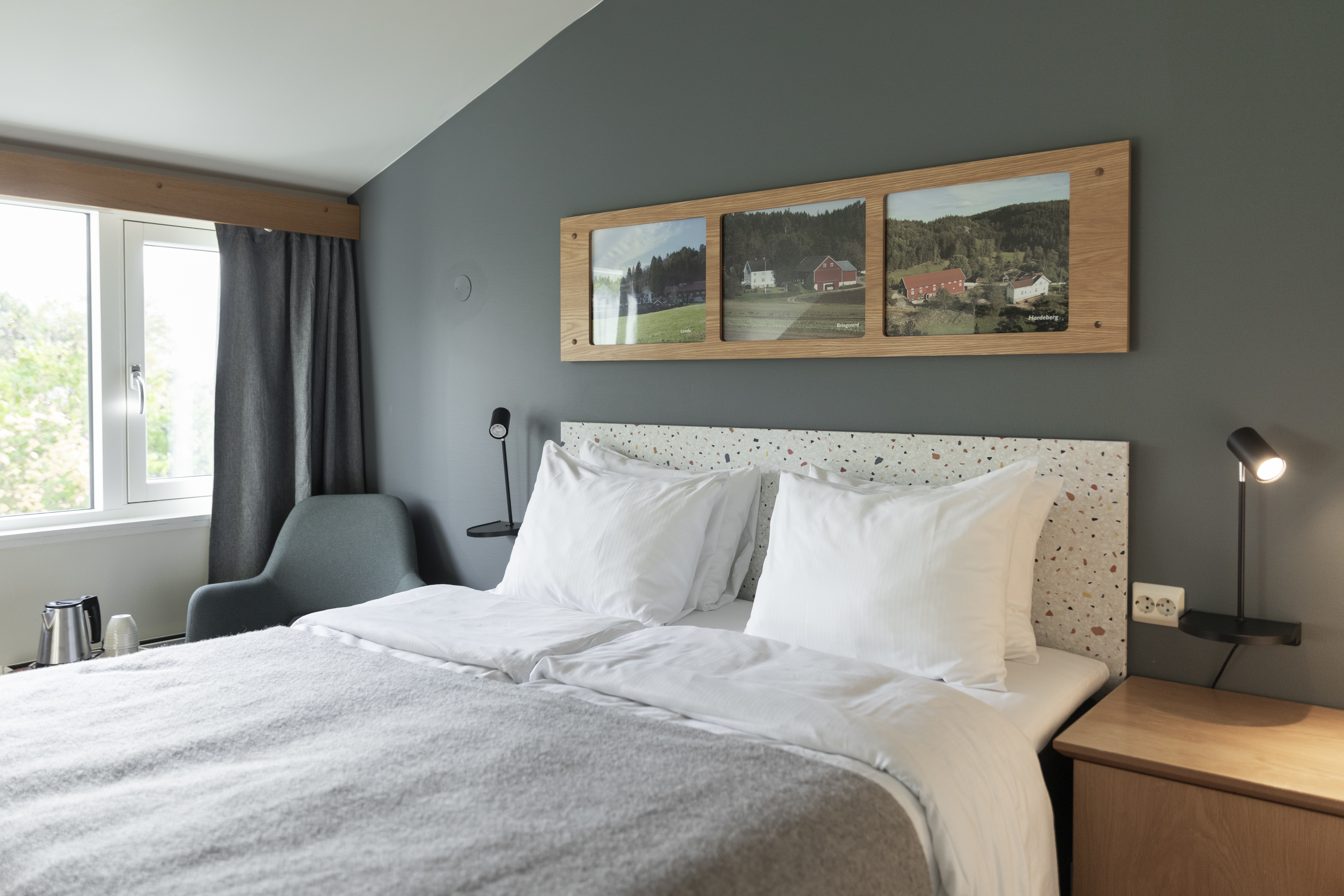 Home Hotel Grimstad Standard Room with soft green and blue colour scheme, large bed, photographs of the area above the headboard, and green trees visible out the window